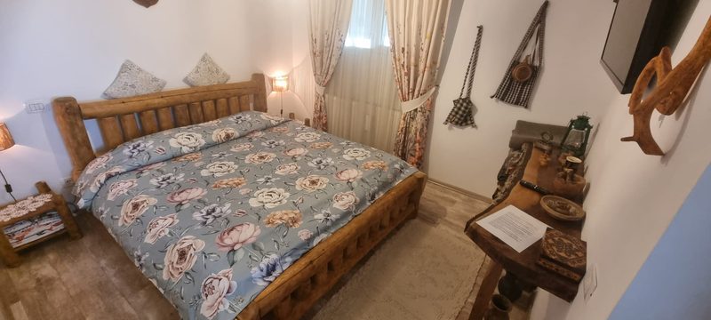 Dormitor cu pat din lemn masiv, lenjerie cu model floral și decorațiuni tradiționale pe perete