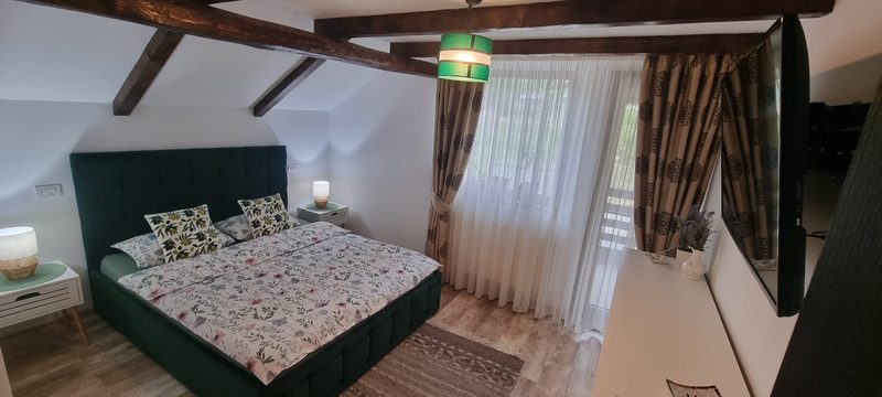 Dormitor cu pat matrimonial, tăblie verde și grinzi de lemn la tavan
