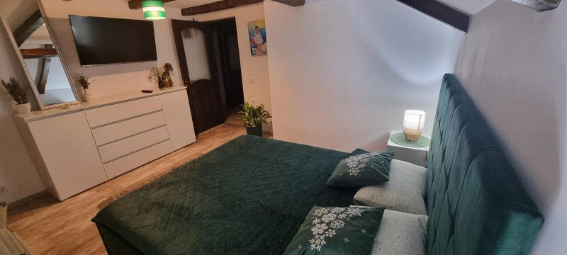 Detaliu din dormitorul verde, cu pat matrimonial, comodă albă și televizor