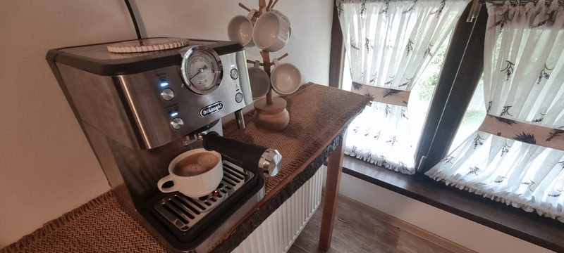 Espressor cu ceașcă de cafea pe blatul de lemn, lângă fereastra bucătăriei