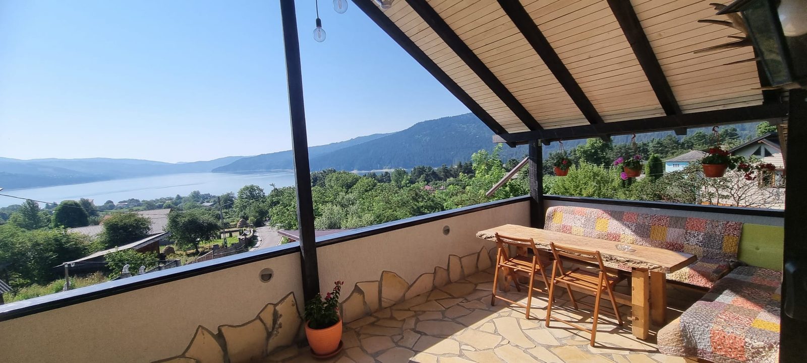 Foișorul acoperit de la Casa David, cu masă lungă de lemn și priveliște deschisă spre Lacul Bicaz și dealurile din jur